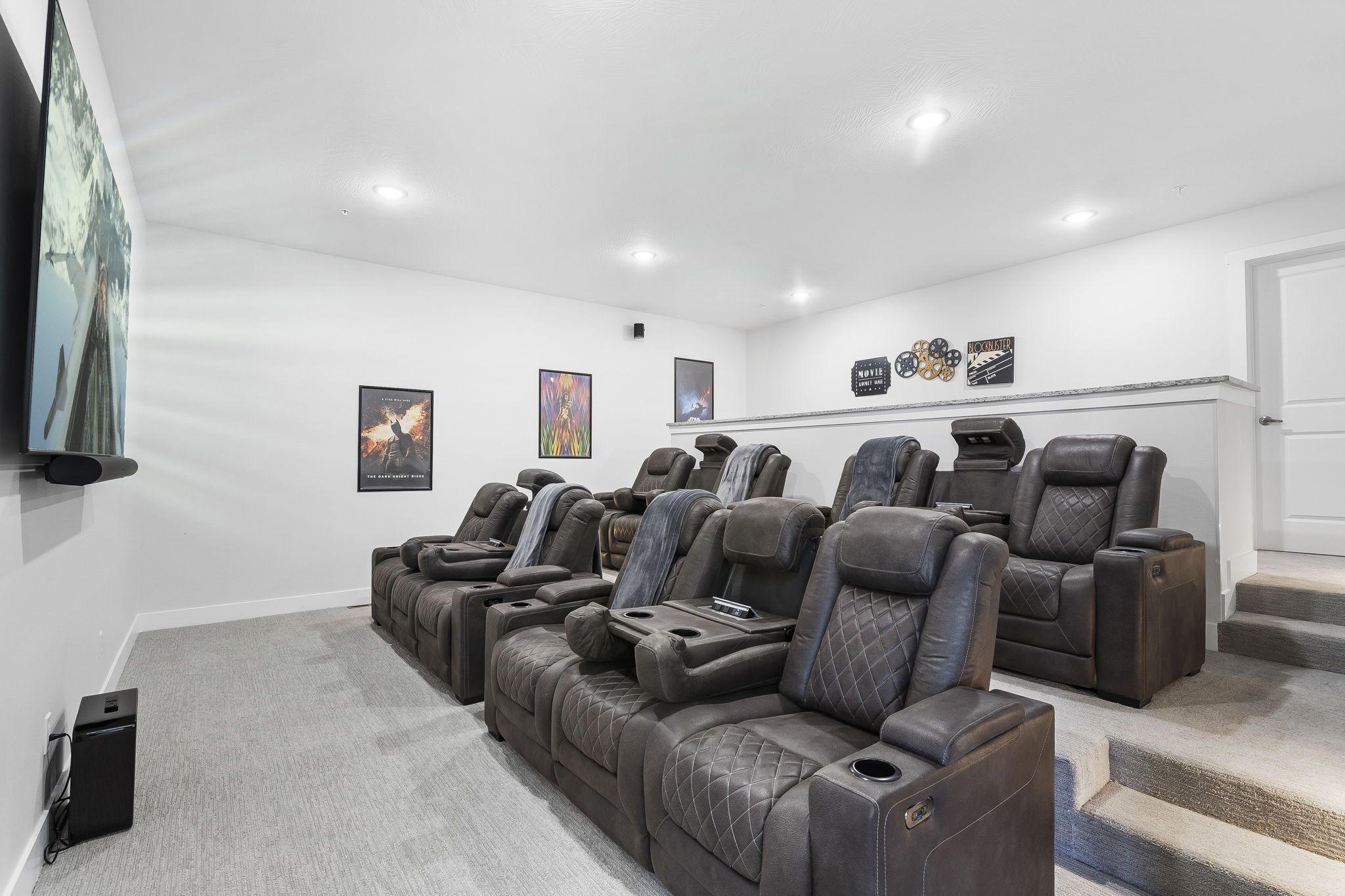 Una sala home theater con diverse poltrone in pelle reclinabili, un'ampia televisione a schermo piatto e poster cinematografici incorniciati alle pareti.