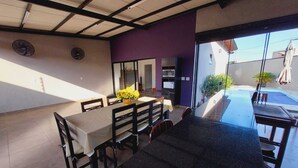 A dining area with a table and chairs, a kitchen area with appliances, and a view of a swimming pool. - Sabe Aquele Lugar Tranquilo e Lindo?! Assim é a Casa de Temporada Analu (Olímpia)