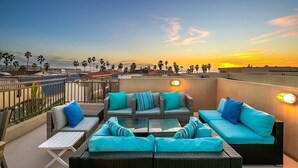 Una terrazza sul tetto con mobili in vimini e cuscini, affacciata su un tramonto e palme.