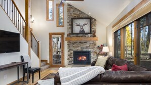 A cozy living room with a stone fireplace, leather sofa, and a flat-screen TV. - Ski Hill Ridge on Peak 7 with Epic Views! (Breckenridge)