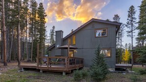 A two-story cabin with a deck, surrounded by tall trees and a sunset sky. - Ski Hill Ridge on Peak 7 with Epic Views! (Breckenridge)