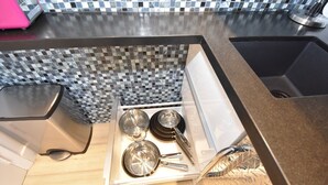 Uma cozinha com painel de backsplash xadrez, uma pia de aço inoxidável e uma gaveta com utensílios de cozinha.