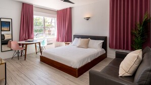 Quarto de hotel moderno com uma cama grande, área de estar com sofá e mesa, e janela com cortinas.