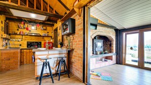 Una cocina acogedora con chimenea de ladrillo, vigas de madera y un amplio ventanal con vistas a un jardín.