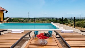 Un área junto a la piscina con cubierta de madera, una mesa con fruteros, dos tazas azules y una toalla.