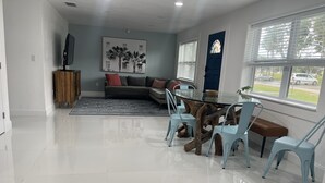 Un salon moderne avec une table à manger au plateau en verre, des chaises bleu clair, un canapé gris et un élément décoratif mural.