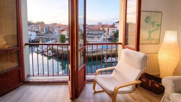 Un balcón con vista a un canal y edificios, una silla blanca y una lámpara.