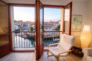 Un balcon donnant sur un canal et des immeubles, une chaise blanche et une lampe.