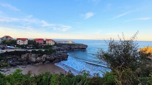 Un pueblo costero con edificios sobre un promontorio rocoso, una playa y el mar.