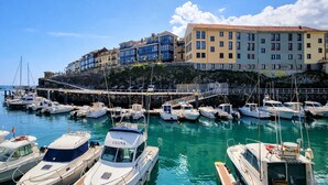 Una marina con varios barcos amarrados, un puente que conecta con edificios y una ladera con construcciones residenciales.