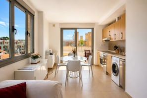 A modern apartment with a dining area, kitchen, and a view of the cityscape.