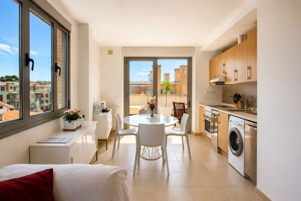 A modern apartment with a dining area, kitchen, and a view of the cityscape.
