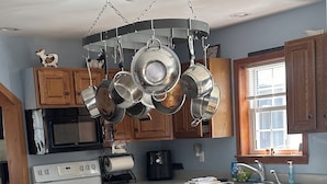 Een keuken met houten kastjes, een roestvrijstalen fornuis, een magnetron en een hangende panrekken.