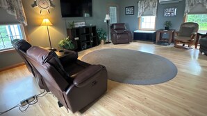 Een ruime woonkamer met een bruine leren fauteuil, een groot rond vloerkleed en een plafondventilator.
