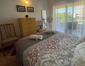 Um quarto com uma cama, cômoda de madeira, cadeira, ventilador e janela com vista.