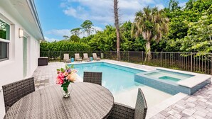 En swimmingpool med flisebelagte kanter, omgivet af et metalhegn og frodig beplantning.
