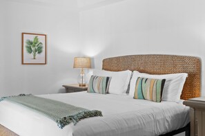 A neatly made bed with a woven headboard, a bedside lamp, and a framed plant on the wall.
