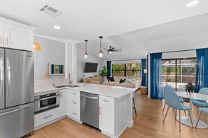A modern kitchen with white cabinets, stainless steel appliances, and a dining area with blue chairs. - Close to Everything! Stylish Home w/ Pool & Spa (Naples)
