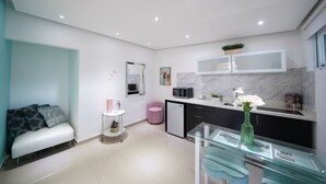 A modern kitchen with a microwave, sink, and a small refrigerator. There is a glass table with a vase of flowers and a bench with cushions.