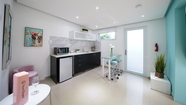 A modern kitchen with a microwave, sink, and cabinets. There is a small table with a glass and a pink box. A plant is on the windowsill.