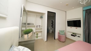A modern bedroom with a bed, a vanity with a mirror, a TV mounted on the wall, and a walk-in closet.