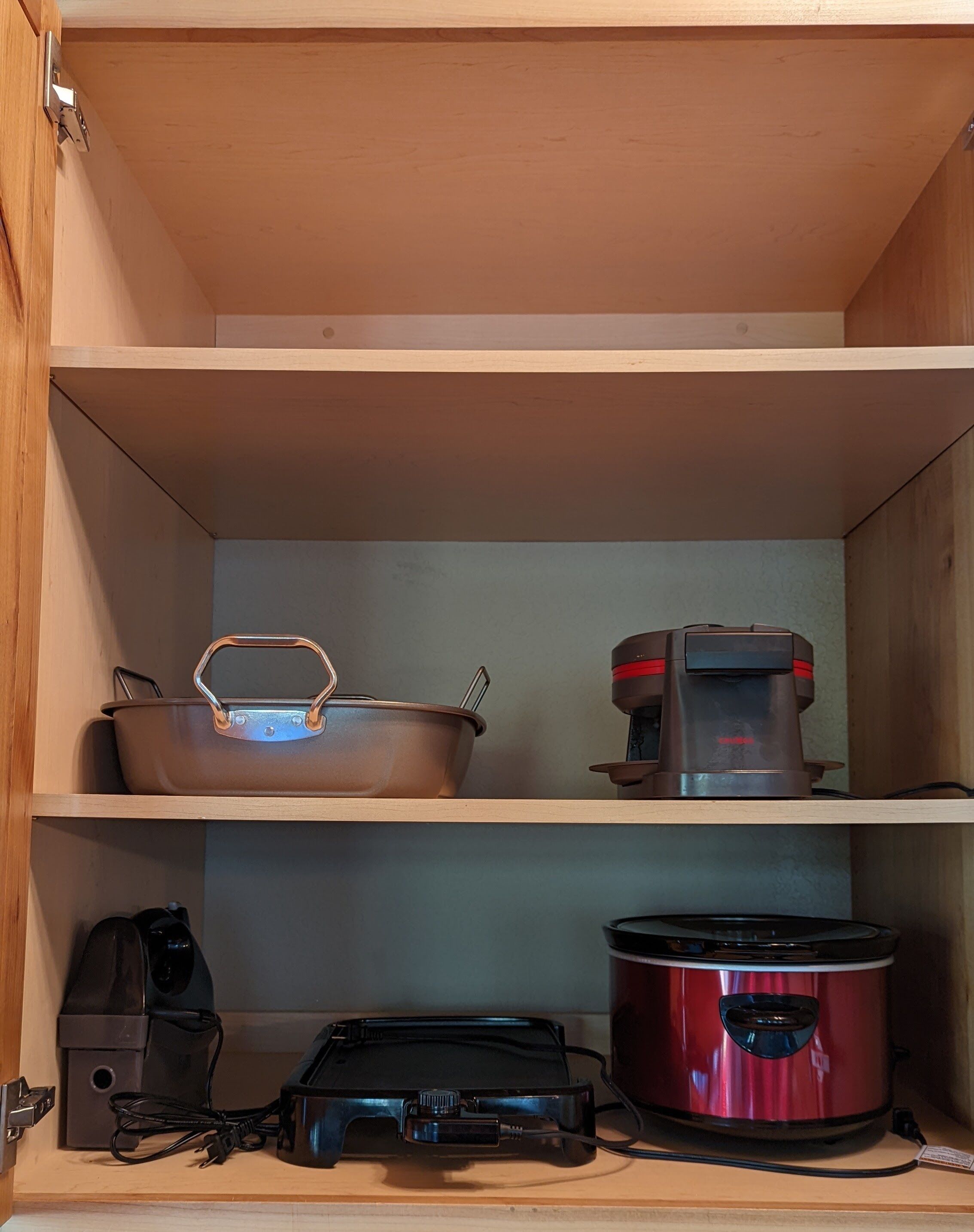 A kitchen with a pot, a coffee maker, and a slow cooker on shelves.