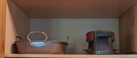 A kitchen with a pot, a coffee maker, and a slow cooker on shelves.