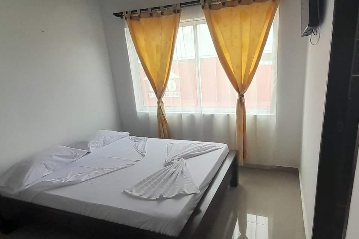 A bedroom with a bed, a window with yellow curtains, and a door leading to another room.