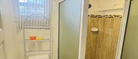 A compact bathroom with a toilet, shower, and storage shelves.