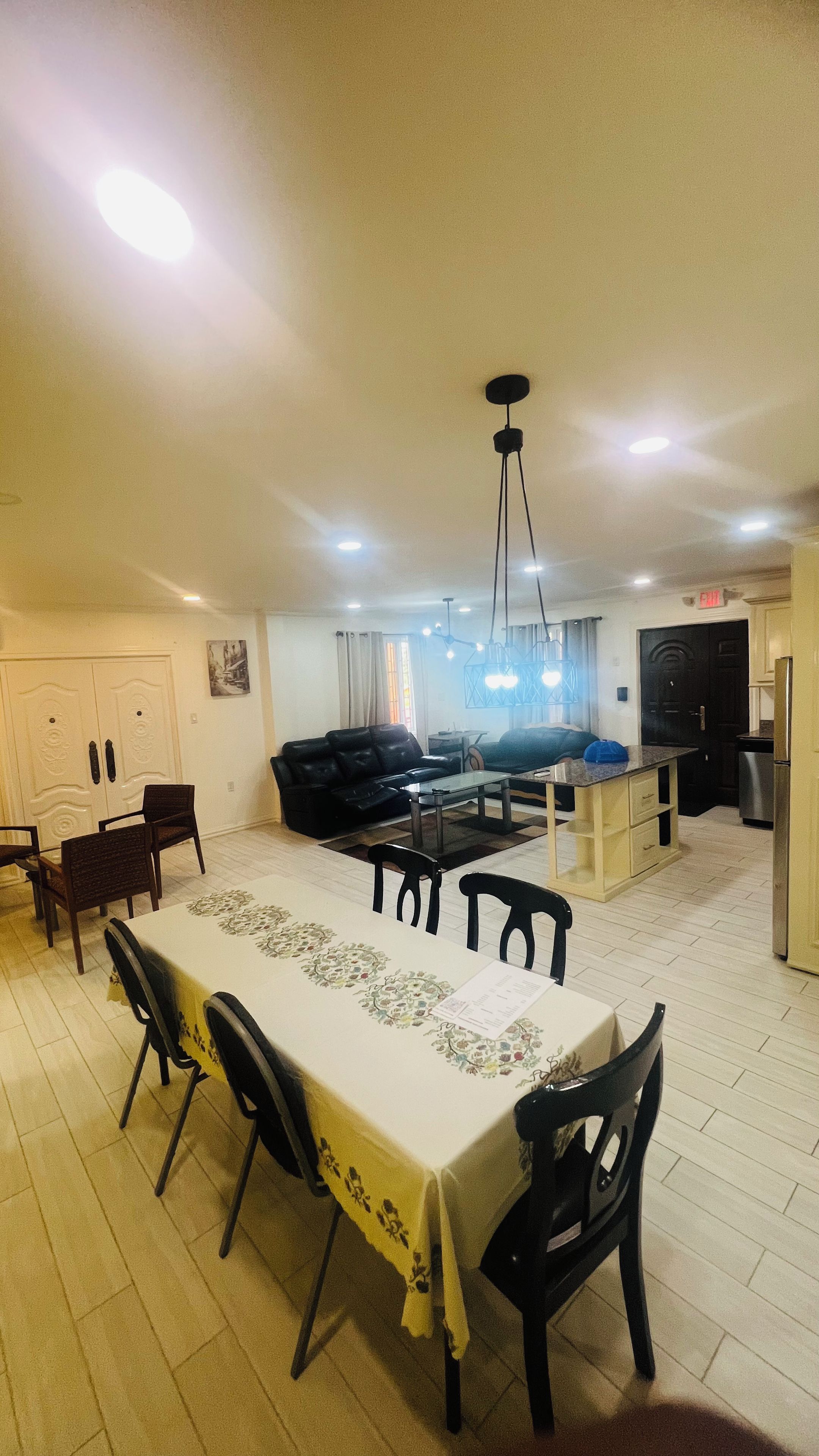Un salón amplio con mesa de comedor, sofás negros y zona de cocina.