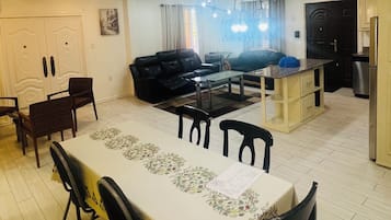 Un salón amplio con mesa de comedor, sofás negros y zona de cocina.