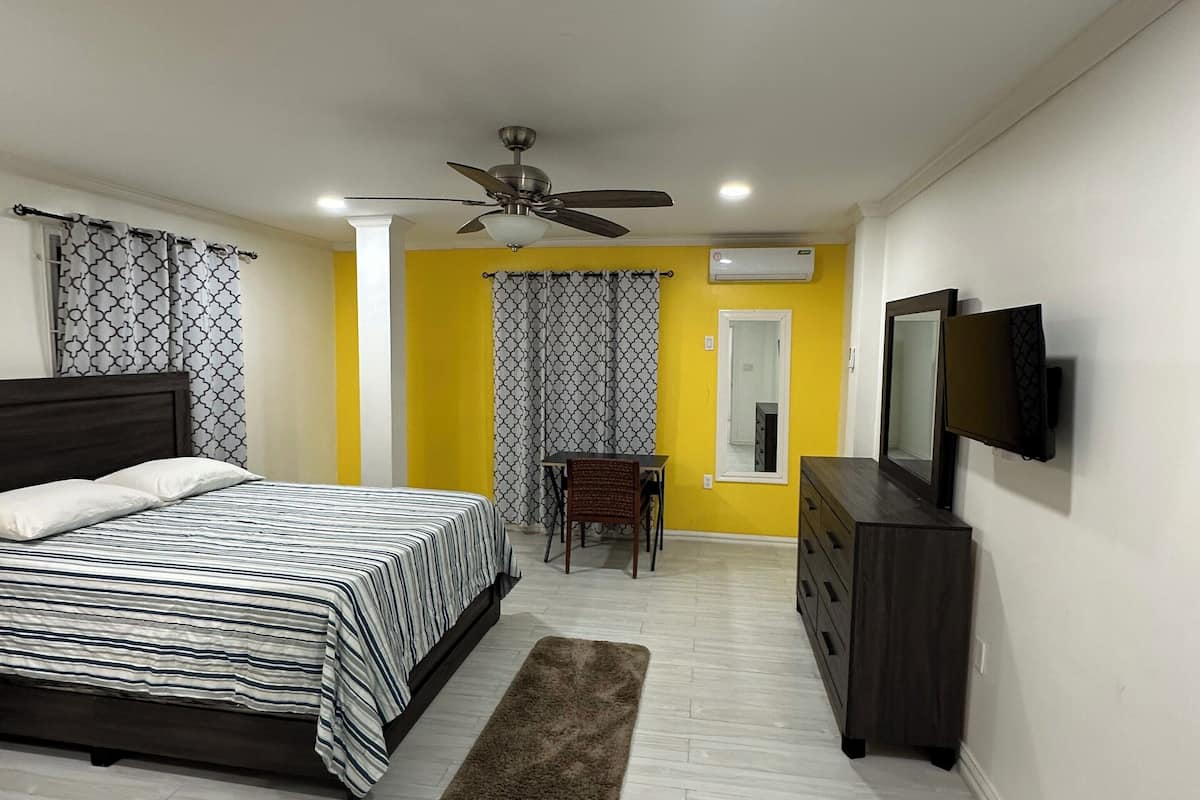 A bedroom with a bed, a dresser, a television, and a ceiling fan.