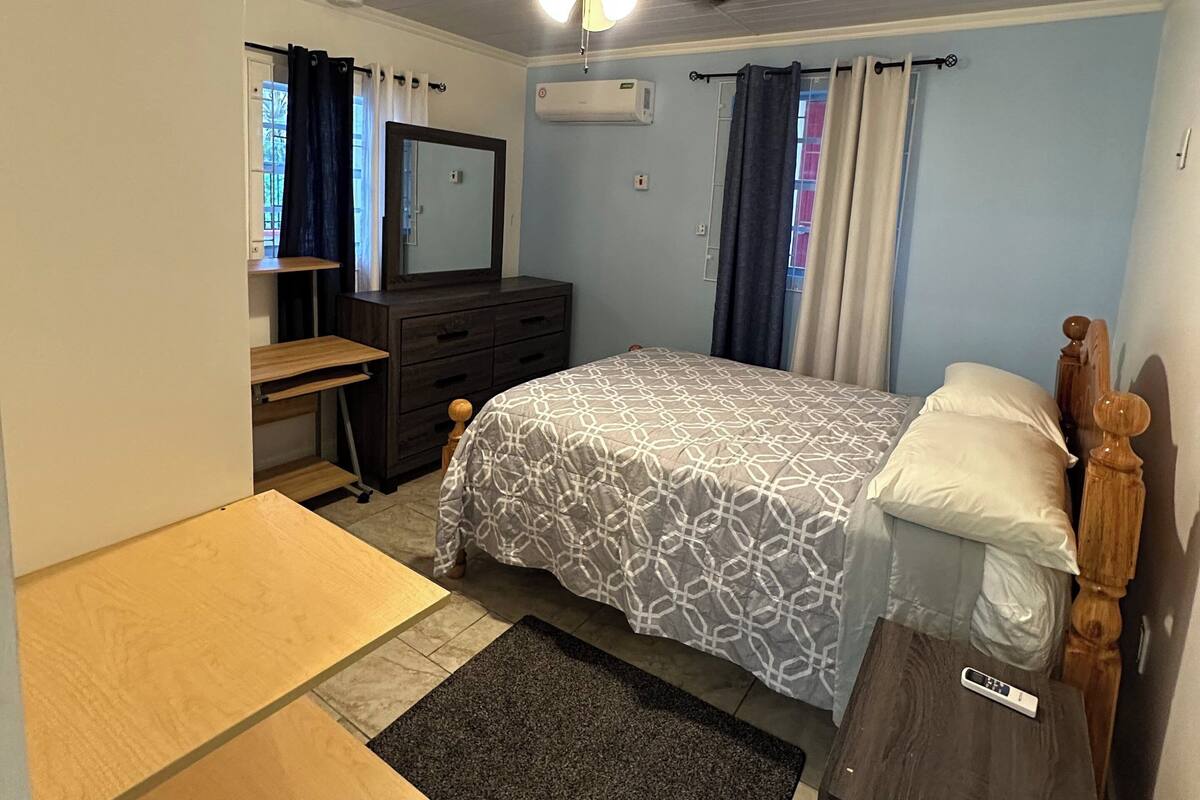A bedroom with a bed, dresser, vanity, and a ceiling fan.