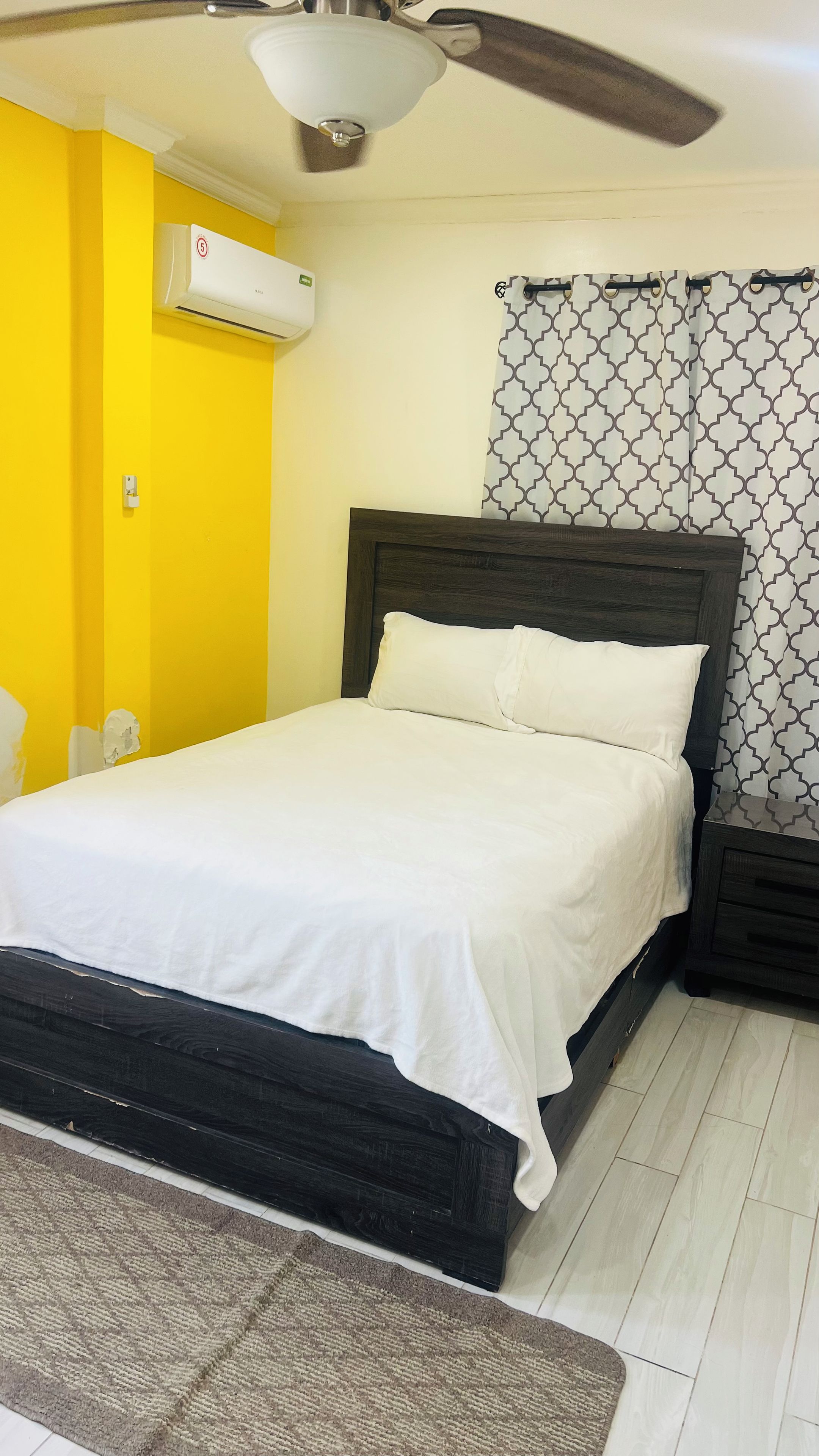 A bed with white bedding, a dark headboard, and a patterned curtain.