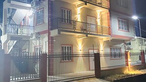Un edificio residencial de varios pisos con balcones, entrada protegida e iluminación exterior.
