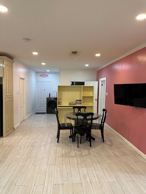 A dining area with a table and chairs, a kitchen area with cabinets, and a TV mounted on the wall. - Your Next Level Int Executive Apartment (Georgetown)