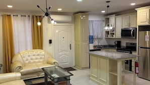 Una cocina moderna con una isla central, un área de comedor con un sofá y una mesa de centro, y una sala de estar con un sofá color beige.