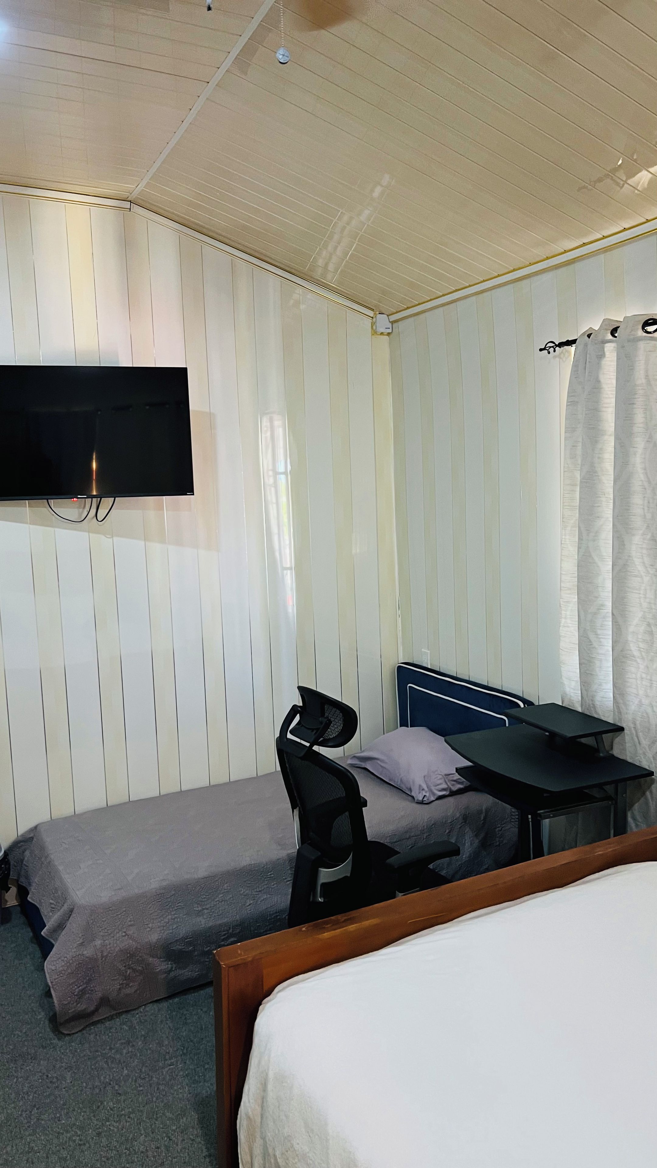 Une chambre avec deux lits simples, un bureau, une chaise, un téléviseur à écran plat et un rideau.