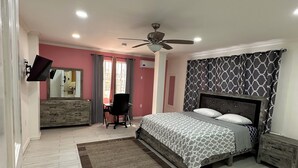 Un dormitorio con cama, escritorio, silla, ventilador de techo y ventana.