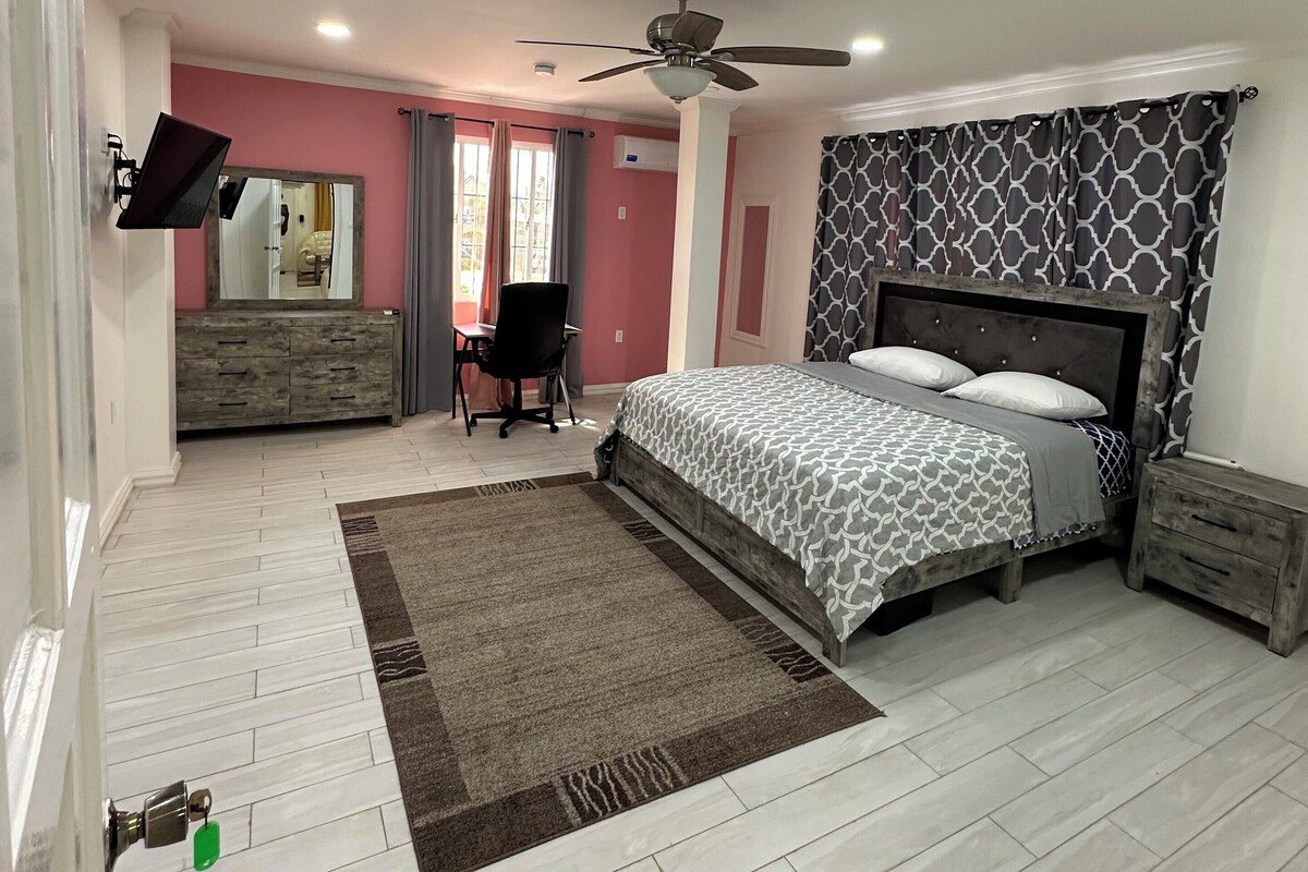 A bedroom with a bed, a desk, a chair, a ceiling fan, and a window.