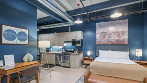 Een moderne hotelkamer met een groot bed, een bureau, een stoel, een kitchenette en een schilderij aan de muur.