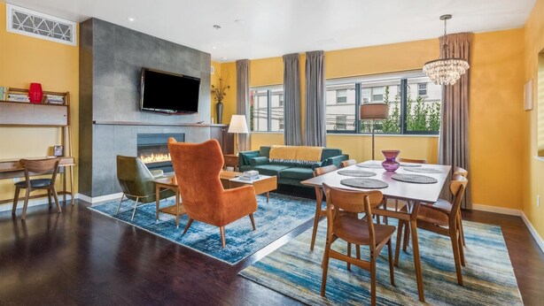 Een moderne woonkamer met een open haard, een flatscreen televisie, een eethoek met een tafel en stoelen, en een groot raam met gordijnen.