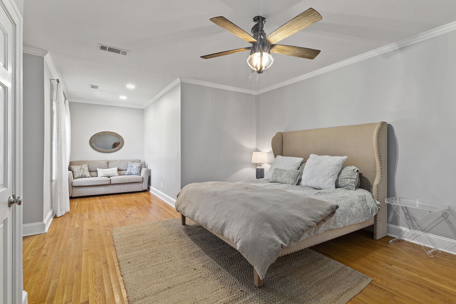 Une chambre à coucher comprenant un lit, un ventilateur de plafond, une table de chevet, une lampe, un miroir et un canapé.
