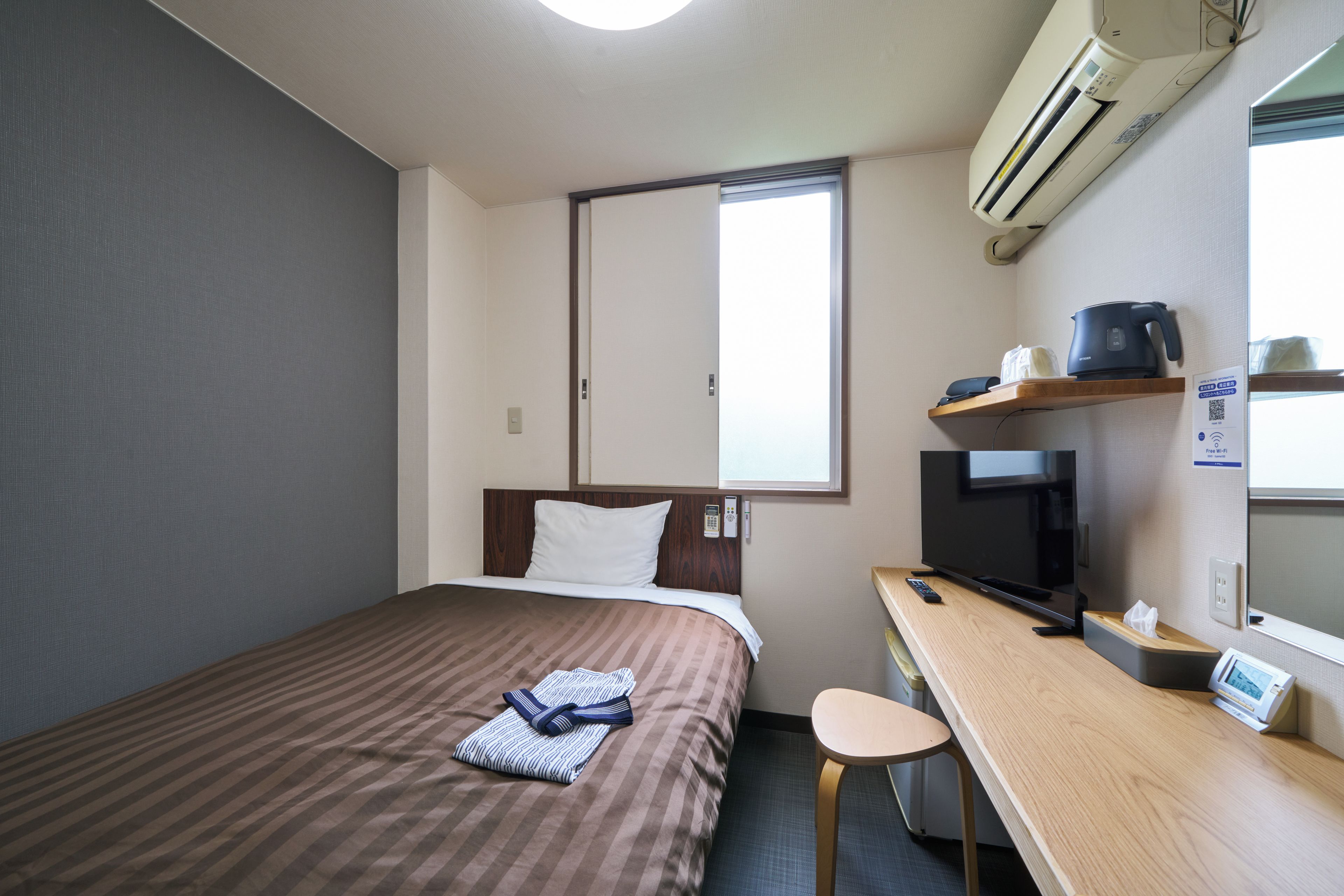 A hotel room with a bed, a desk, a television, and a window.