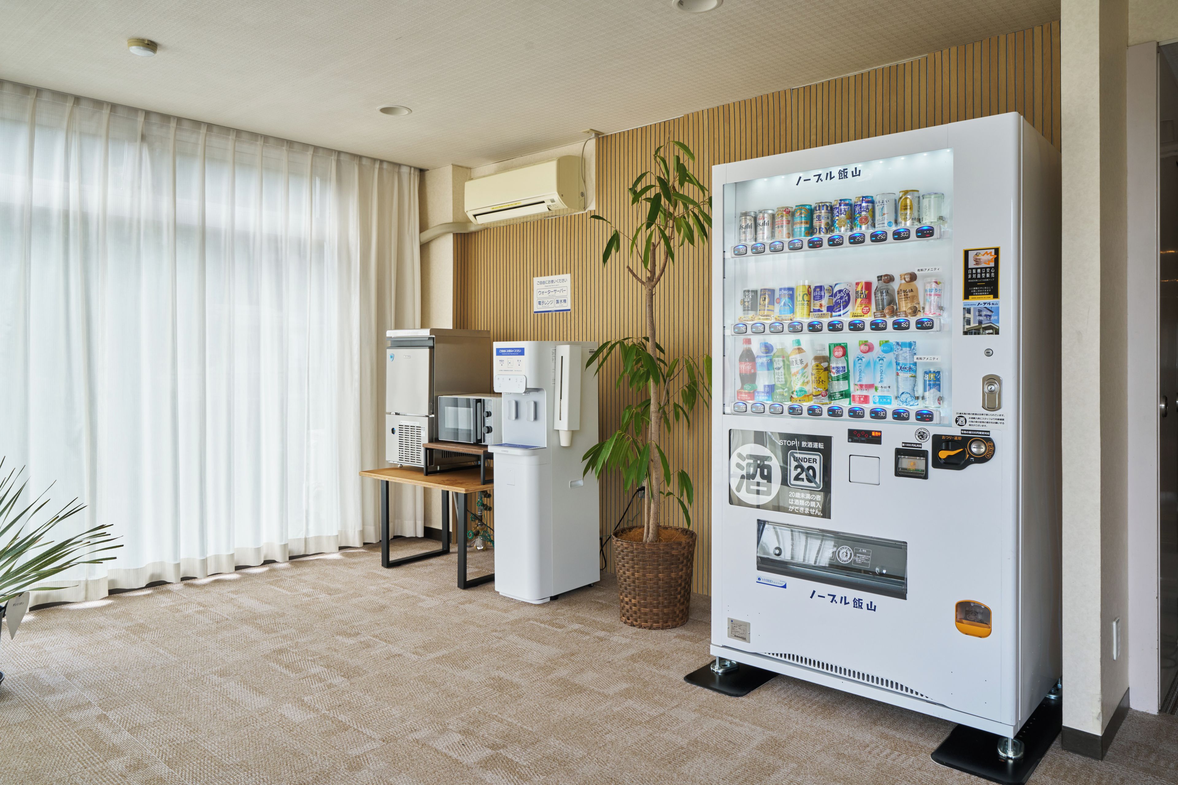 Hotellihuone, jossa on minibaari, mikroaaltouuni, jääkaappi, kasvi ja suuri ikkuna, jossa on verhot.