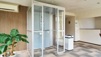 Un espacio de oficina moderno con un divisor de vidrio, una planta en maceta y un purificador de aire blanco.