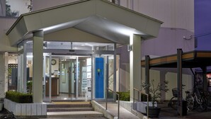A hotel entrance with a covered entrance, glass doors, a clock, and a blue door. - Hotel Noble Iiyama (Iiyama)
