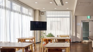 A spacious room with wooden tables and chairs, a flat-screen TV, and large windows with sheer curtains. - Hotel Noble Iiyama (Iiyama)