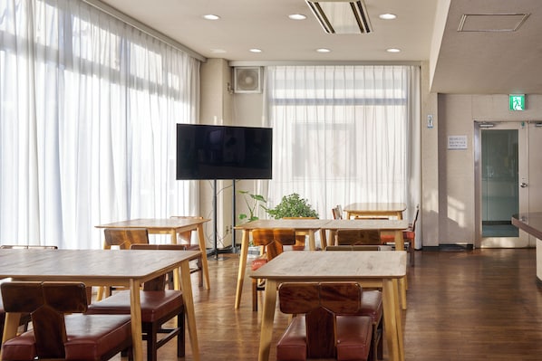A spacious room with wooden tables and chairs, a flat-screen TV, and large windows with sheer curtains. - Hotel Noble Iiyama (Iiyama)