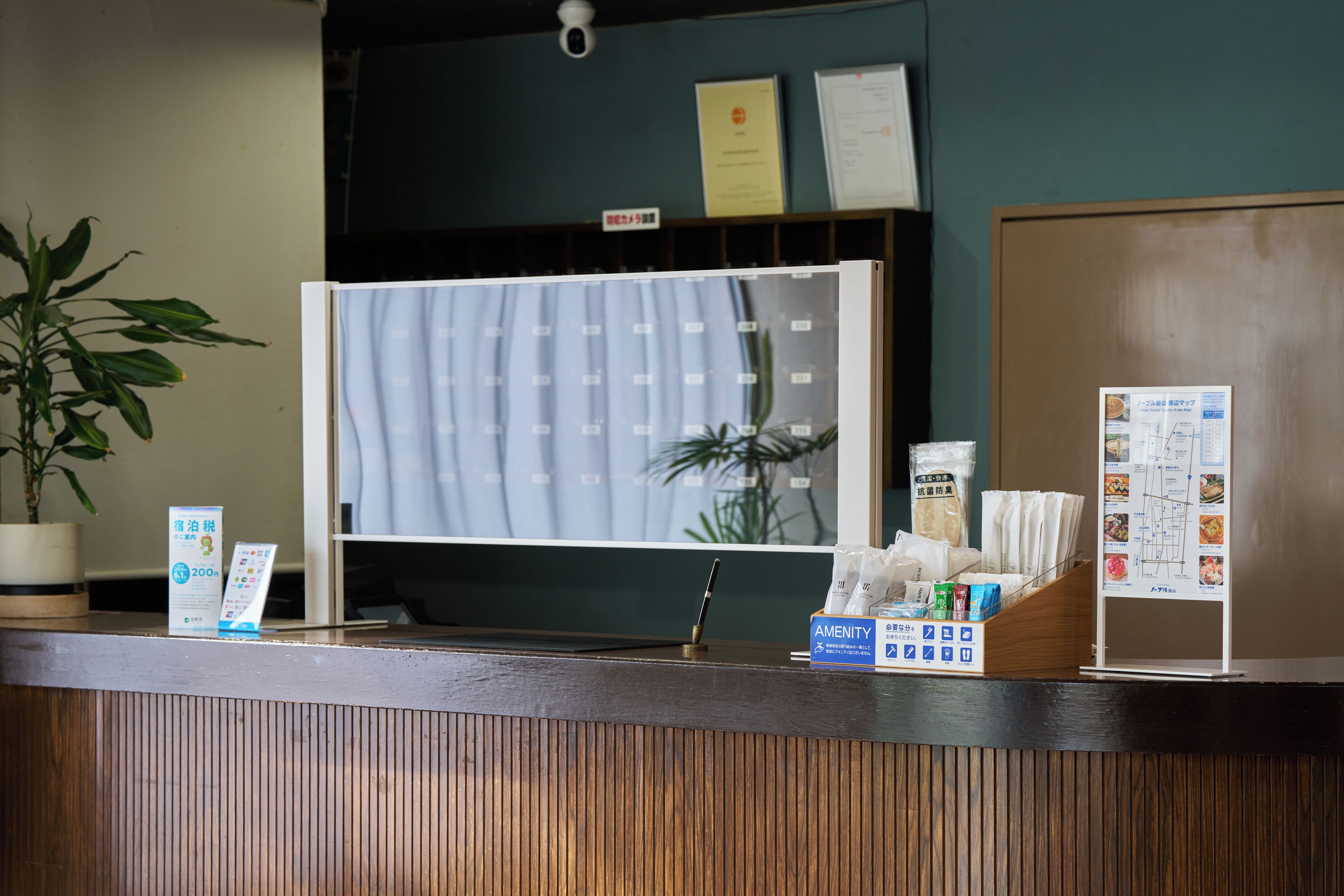 A hotel reception desk with a plant, a menu stand, and a sign indicating amenities.
